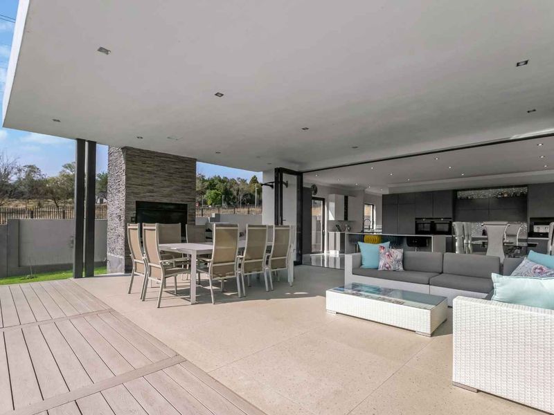 Spacious covered patio featuring a built-in fireplace with stone cladding, seamless indoor-outdoor flow through bi-fold doors, and a mix of tiled and timber decking.