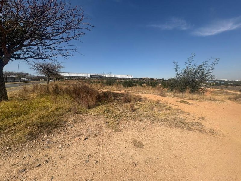 An expansive, undeveloped industrial land plot featuring natural vegetation and a dirt access path, offering significant potential for future development.