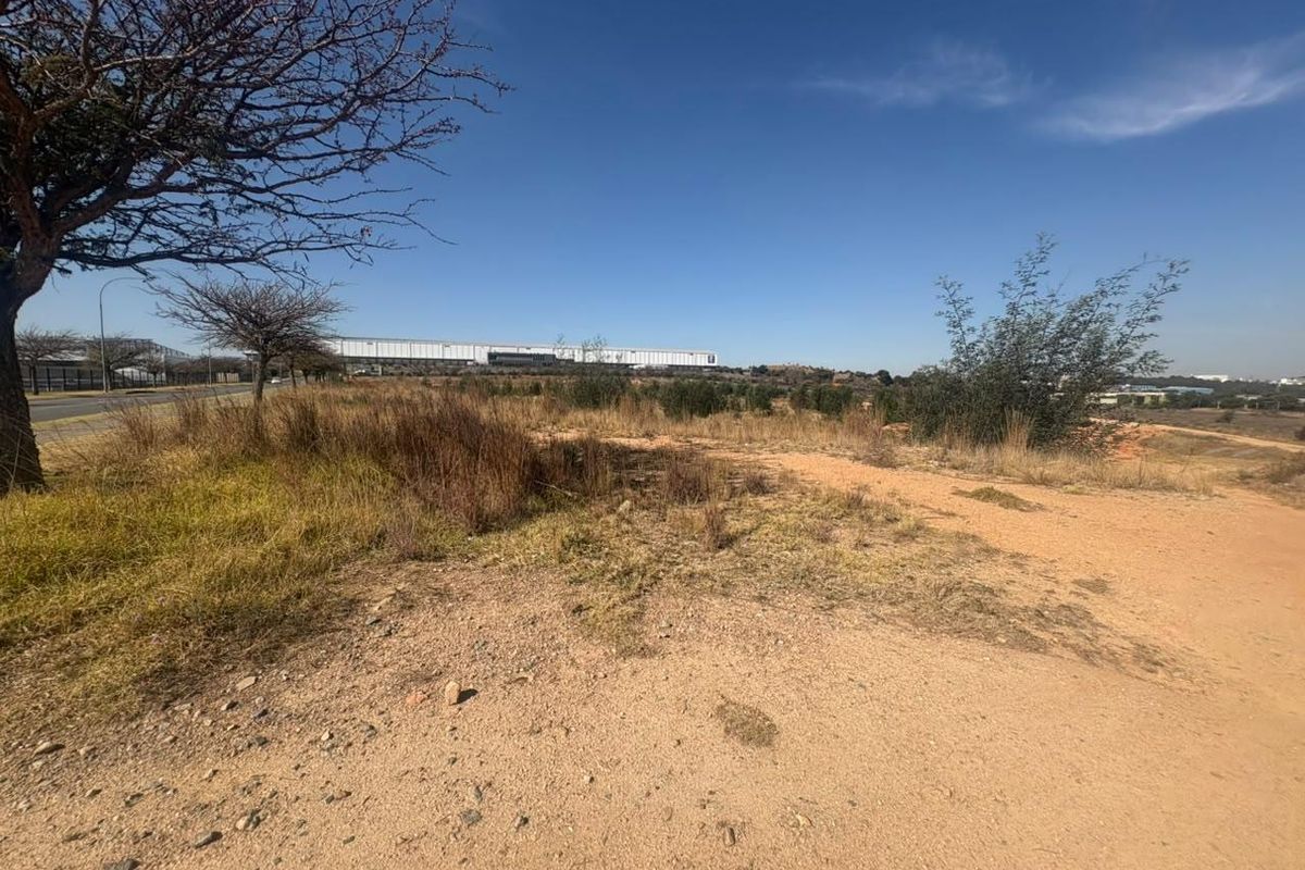An expansive, undeveloped industrial land plot featuring natural vegetation and a dirt access path, offering significant potential for future development.