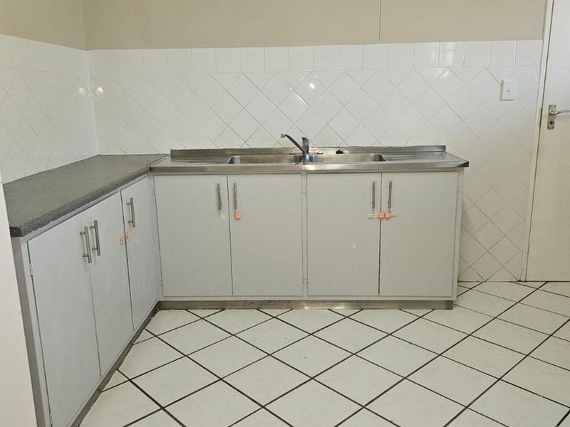 A functional, empty kitchen featuring tiled flooring, a tiled backsplash, and basic cabinetry with a stainless steel double sink.