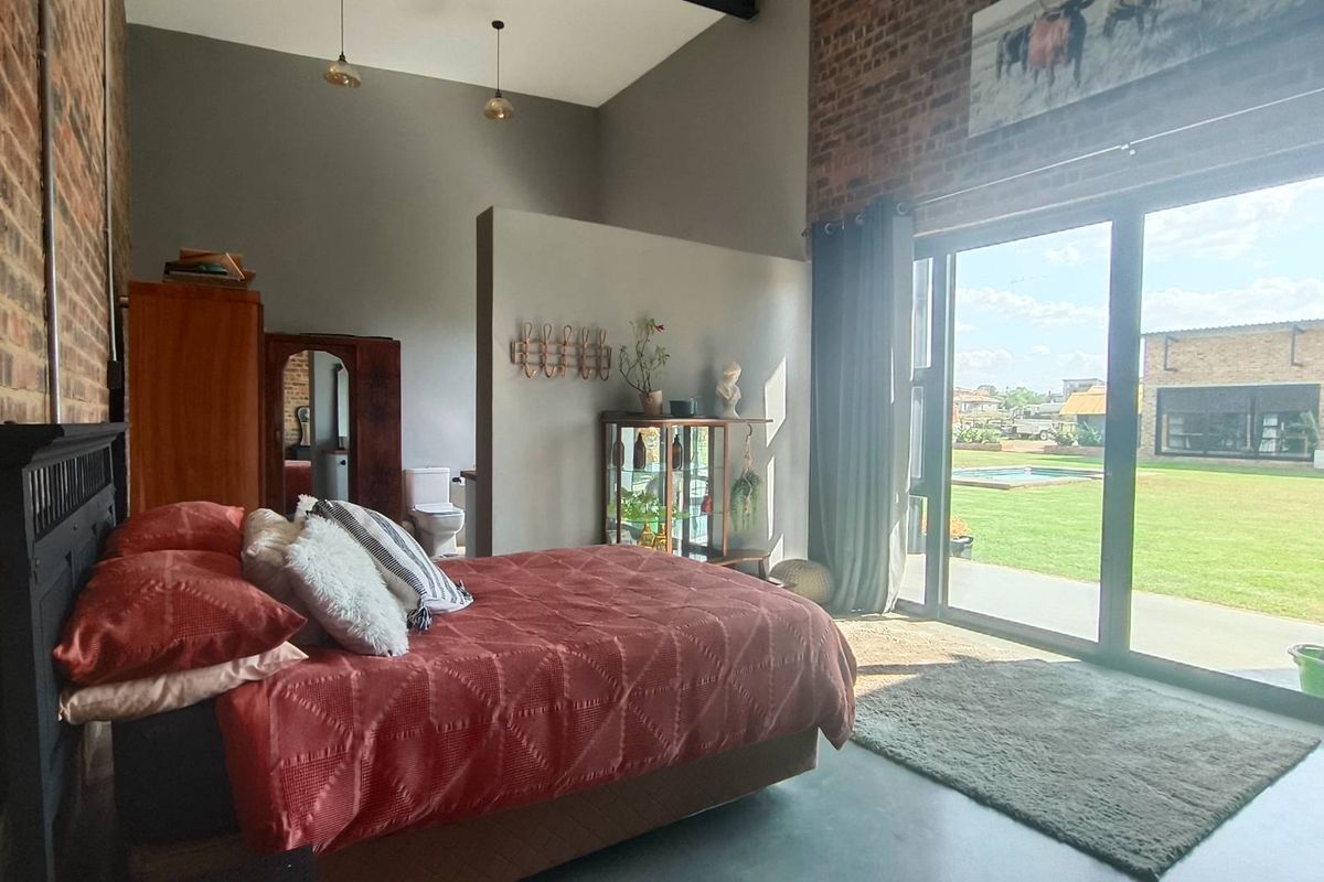 Spacious bedroom featuring exposed brick walls, high vaulted ceilings, and large sliding glass doors opening onto a private garden and pool area.