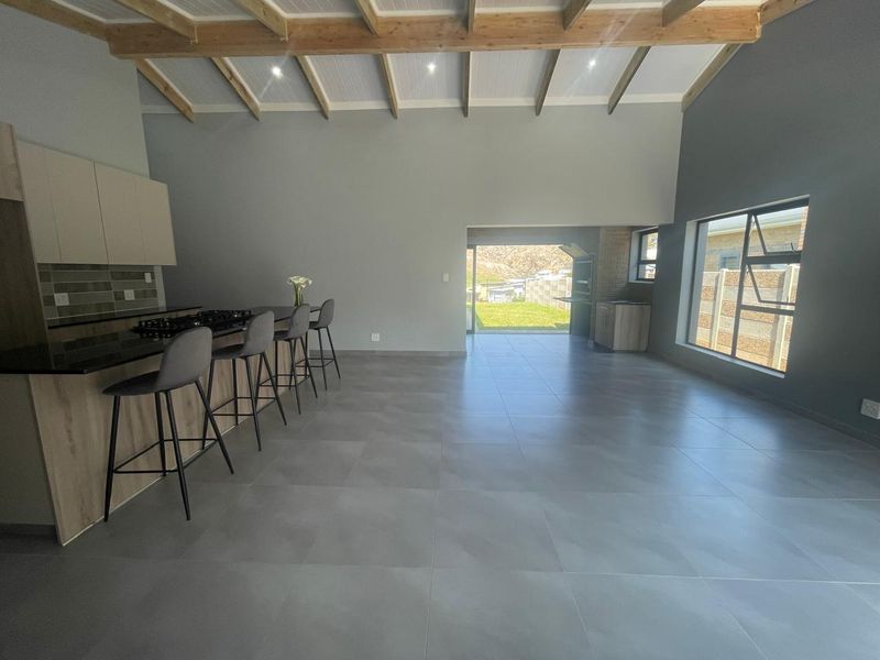 Spacious open-plan living area featuring exposed timber beams, modern kitchen with granite countertops, gas hob, and seamless flow to the outdoor patio area.