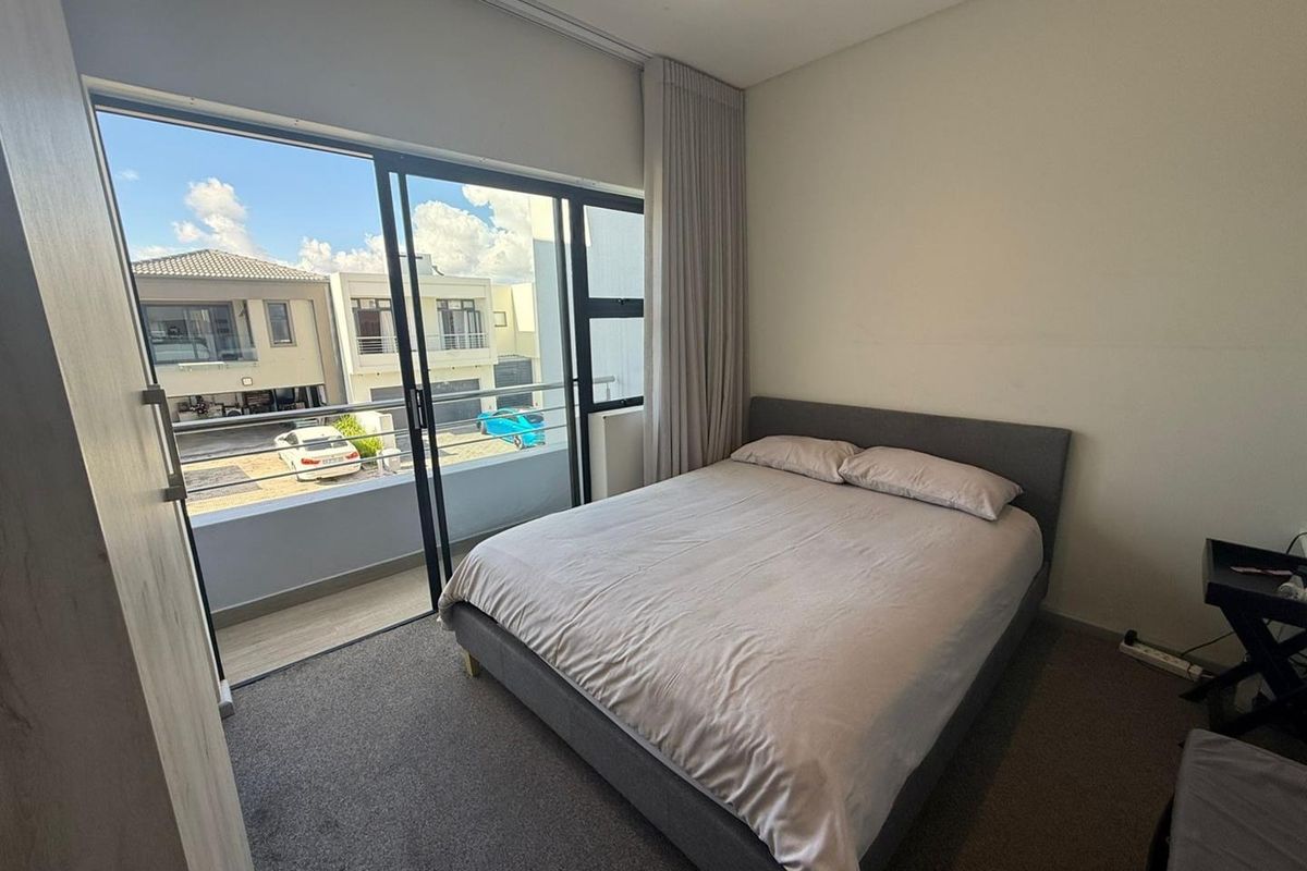 A bright bedroom featuring neutral carpeting, built-in curtain tracks, and a large sliding glass door providing access to a private balcony.