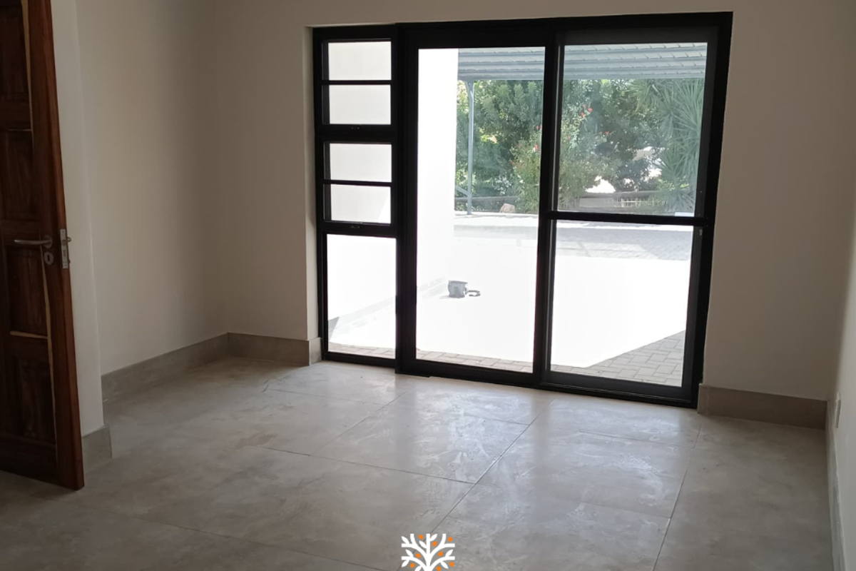 An empty room featuring large black-framed sliding glass doors that open onto an outdoor patio area, with neutral tiled flooring throughout.