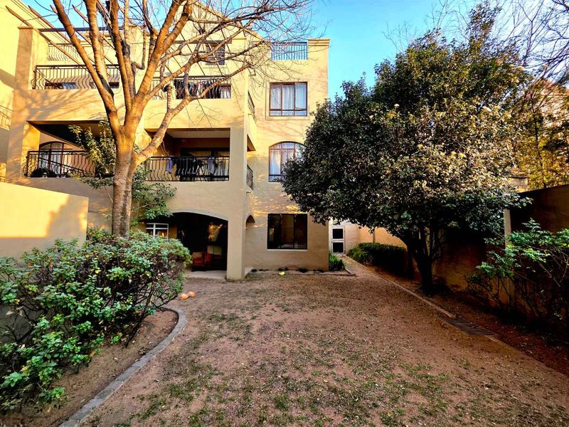 Rear view of a multi-story apartment building featuring private balconies with wrought iron railings, arched windows, and a shared garden area.