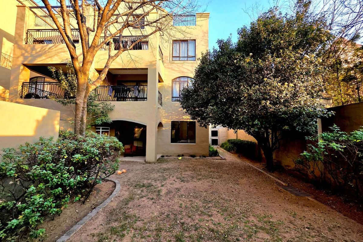 Rear view of a multi-story apartment building featuring private balconies with wrought iron railings, arched windows, and a shared garden area.