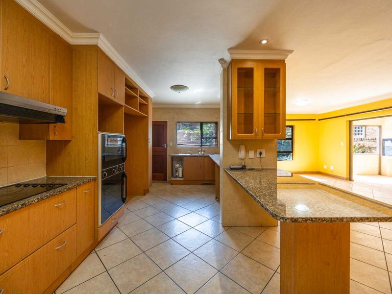Open-plan kitchen featuring wooden cabinetry, granite countertops, and integrated appliances, flowing into a bright living area with direct access to the patio.
