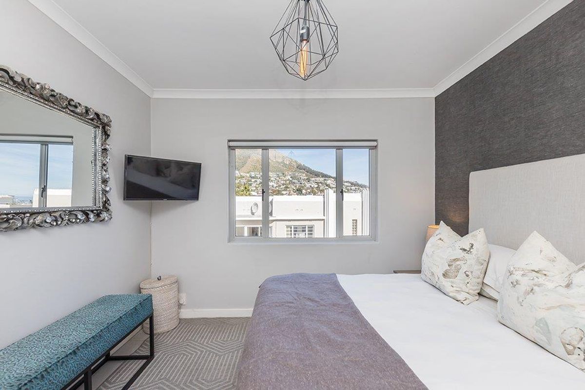A well-maintained bedroom featuring a textured accent wall, neutral carpeting, and a window offering mountain and urban views.