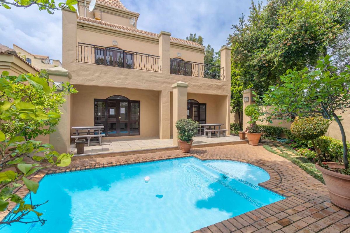 Rear view of the apartment featuring a covered patio, a private swimming pool, and a balcony with wrought iron railings overlooking the garden.
