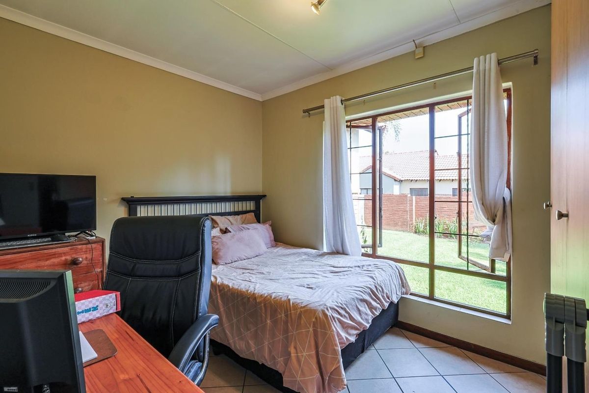 A functional bedroom featuring tiled flooring, large windows with garden views, and built-in storage space.
