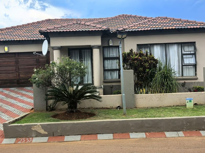 Front elevation of a single-story house featuring a tiled roof, double garage, and a paved driveway with a low boundary wall.