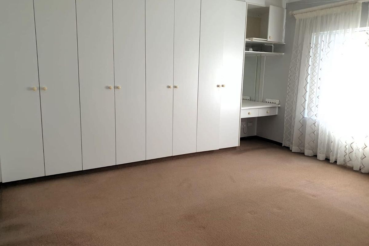 A spacious bedroom featuring extensive built-in white cabinetry with an integrated vanity area and neutral carpeting.