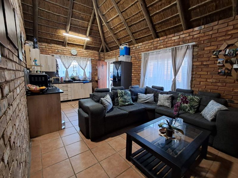 Open-plan living area featuring exposed brick walls, a high thatched ceiling, and a functional kitchen space with tiled flooring throughout.