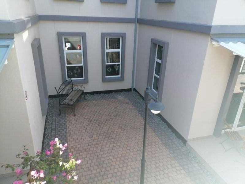 A paved rear courtyard area featuring exterior lighting and access to the office building through multiple windows.