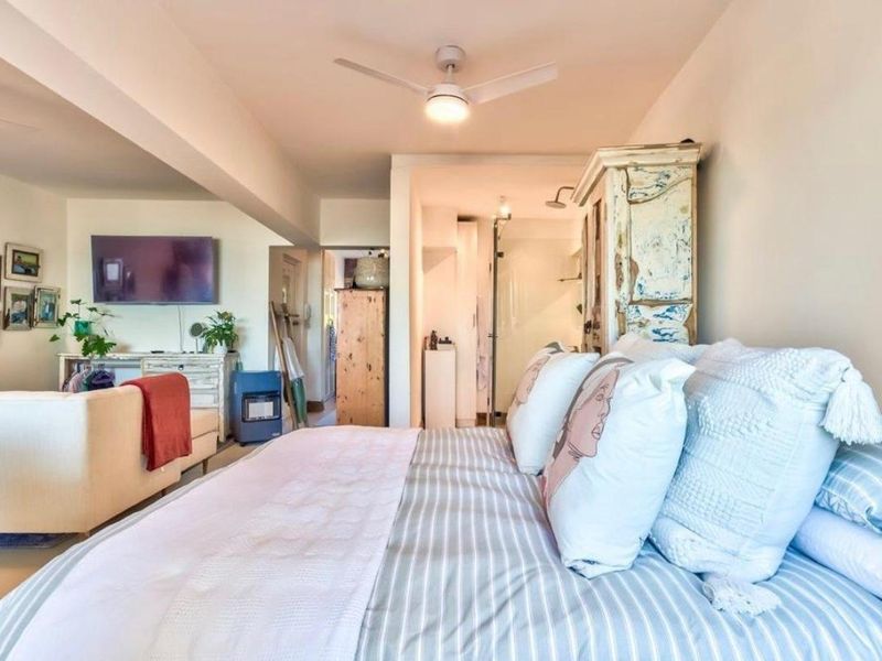 A bedroom featuring a ceiling fan and direct access to an en-suite bathroom, with an open-plan layout connecting to the living area.