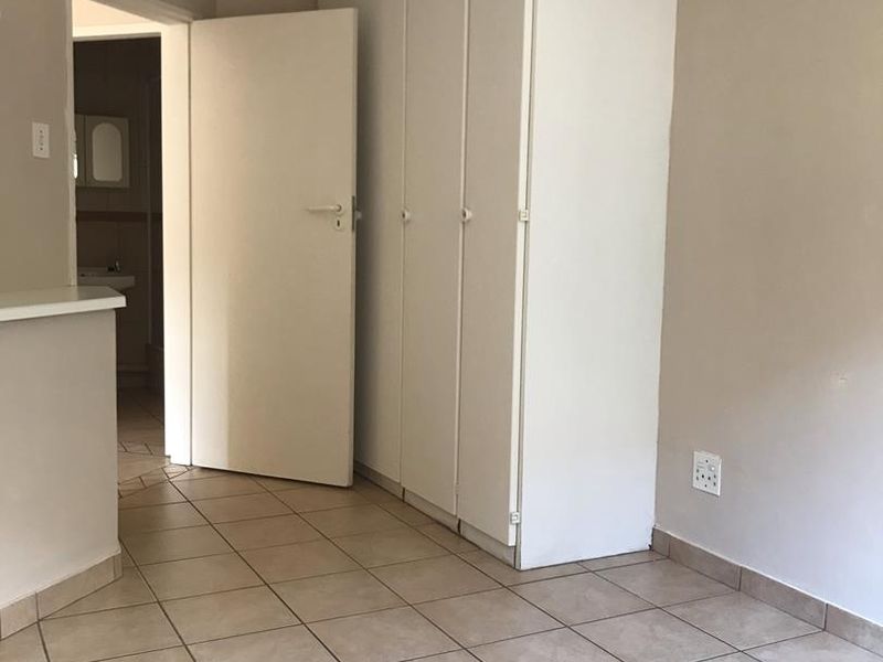 A clean, empty bedroom featuring neutral wall tones, tiled flooring, and ample built-in cupboard storage, with direct access to an adjoining bathroom.