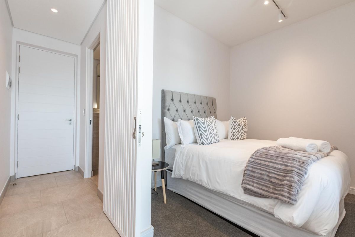A modern, well-maintained bedroom featuring a slatted room divider, recessed downlights, and a combination of tiled and carpeted flooring.