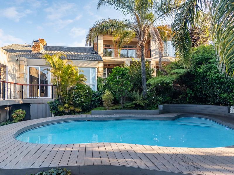 A well-maintained backyard featuring a swimming pool with composite decking, a raised balcony, and established garden landscaping.