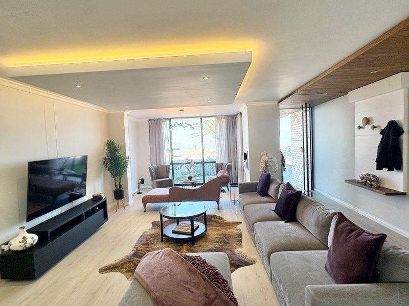 Spacious living room featuring a modern recessed ceiling with ambient LED lighting, timber accents, and large sliding doors leading to an outdoor area.