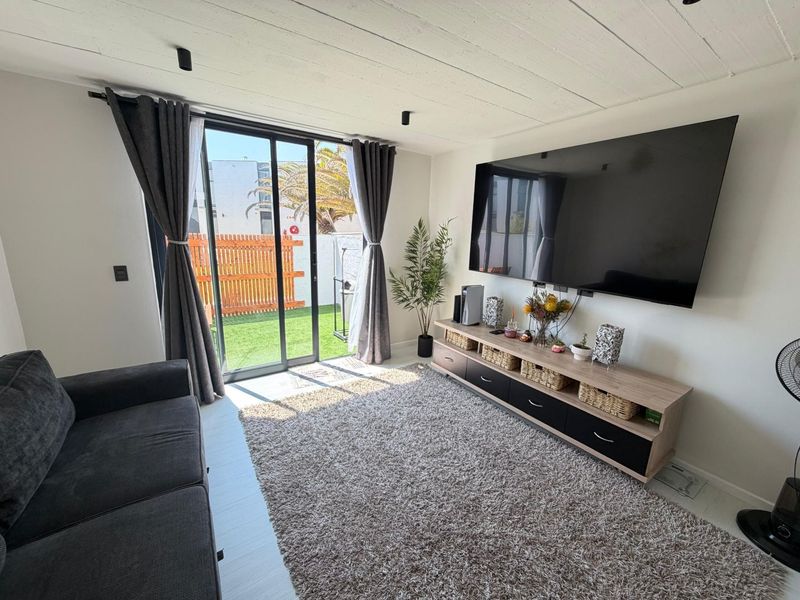 Modern living room featuring an exposed concrete ceiling, recessed lighting, and large sliding glass doors providing direct access to a private outdoor area.