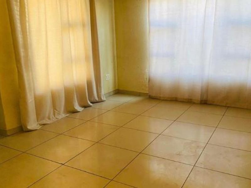 An empty living room featuring tiled flooring and large windows with curtains, providing a blank canvas for potential interior design updates.