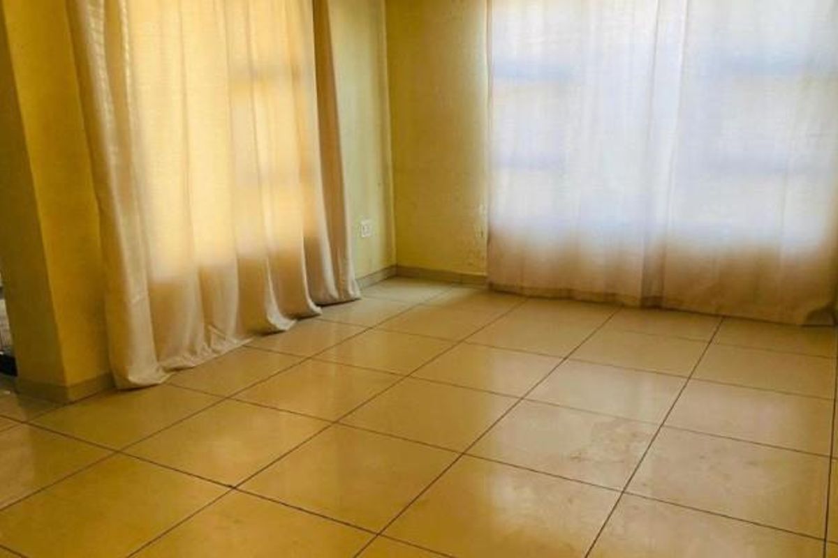 An empty living room featuring tiled flooring and large windows with curtains, providing a blank canvas for potential interior design updates.