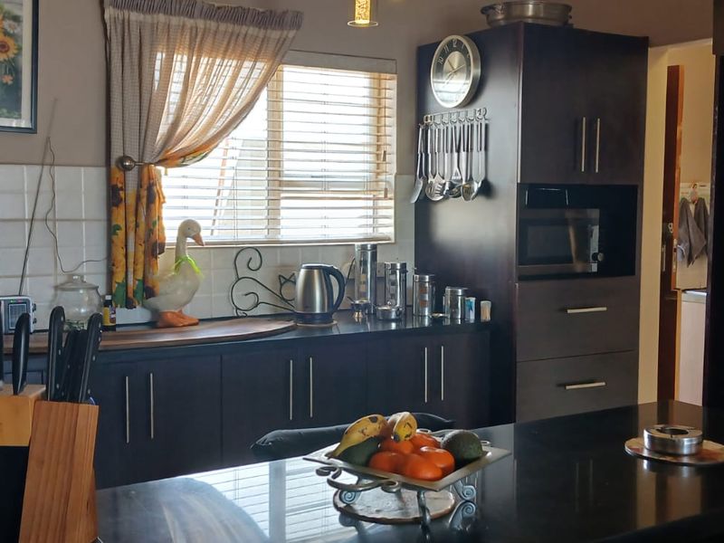 A functional kitchen featuring dark wood cabinetry, a central island with stone countertops, built-in appliances, and a tiled backsplash.