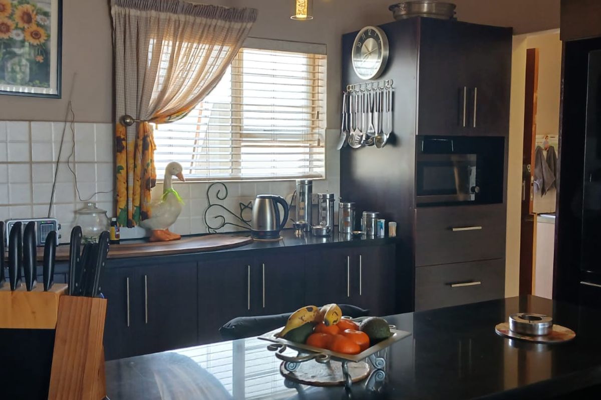 A functional kitchen featuring dark wood cabinetry, a central island with stone countertops, built-in appliances, and a tiled backsplash.