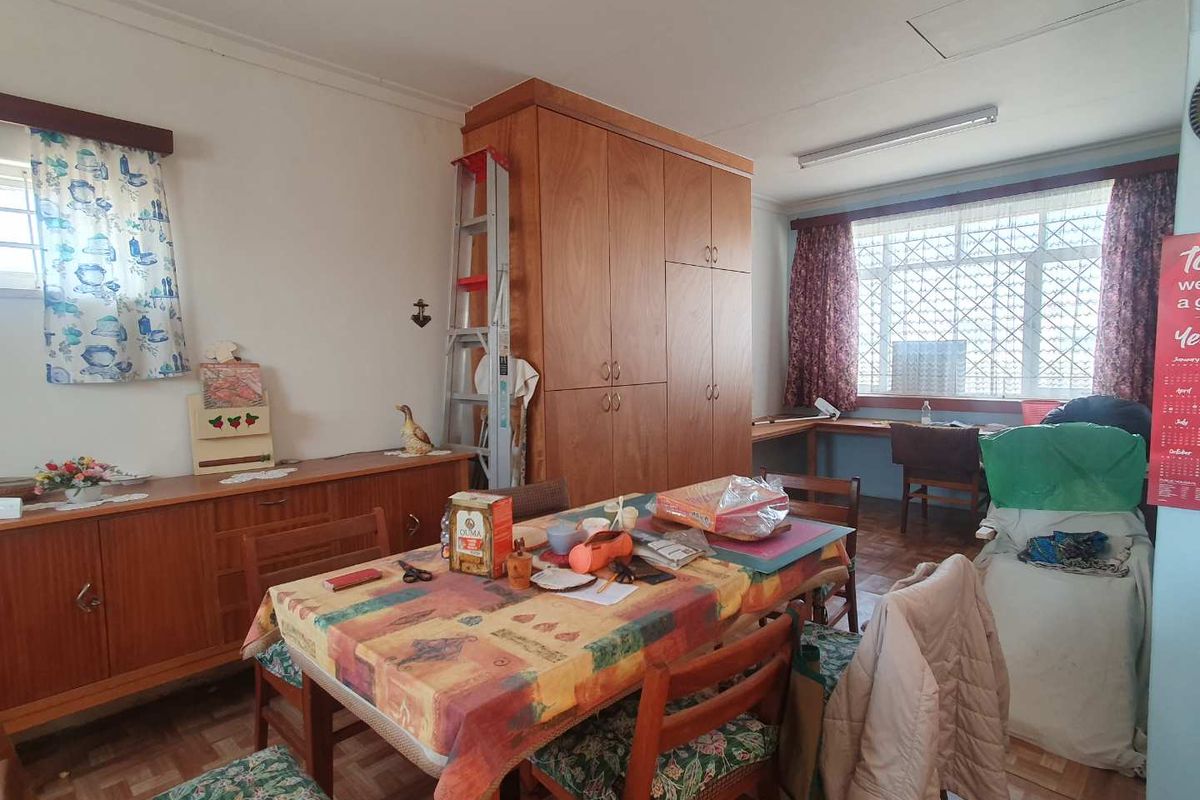 A multi-purpose living area featuring built-in wooden cabinetry, parquet flooring, and large windows with security bars, offering a functional space for dining or study.
