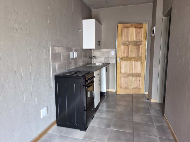 A compact, functional kitchen area featuring tiled flooring, basic cabinetry, a stove, and a tiled backsplash, currently in a shell-like condition.