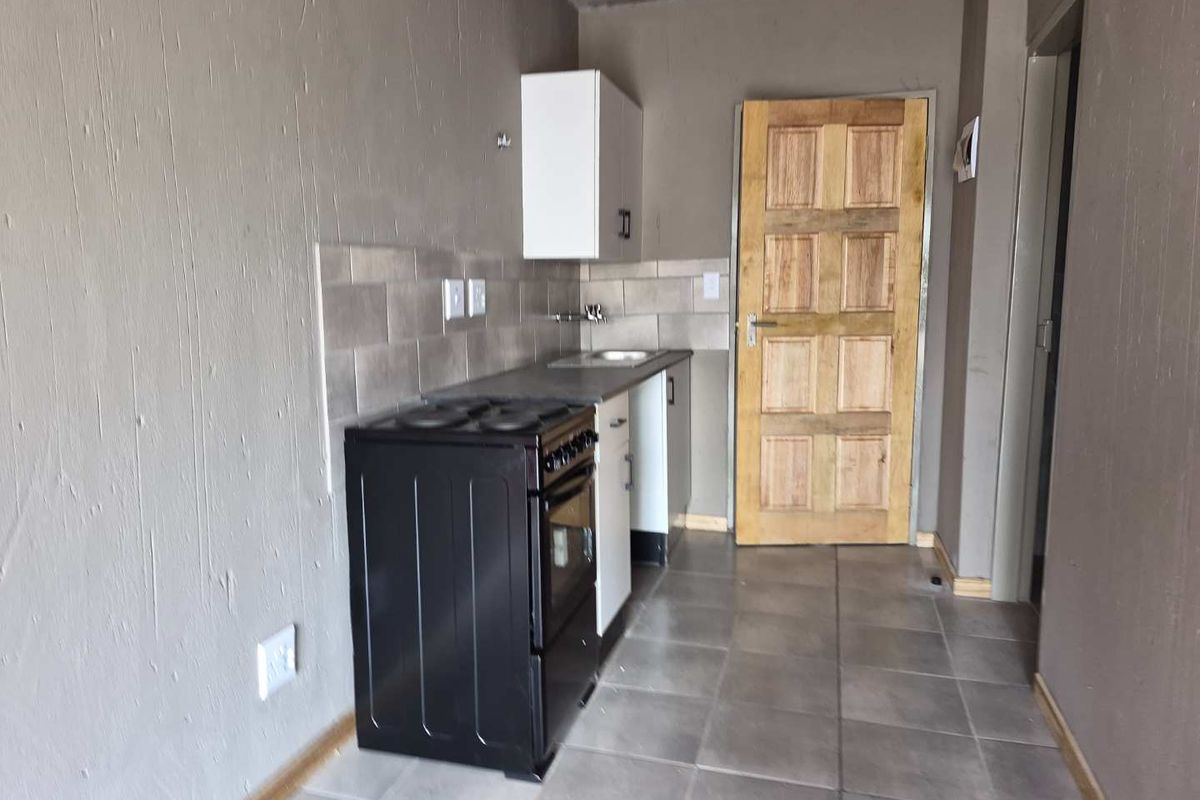 A compact, functional kitchen area featuring tiled flooring, basic cabinetry, a stove, and a tiled backsplash, currently in a shell-like condition.