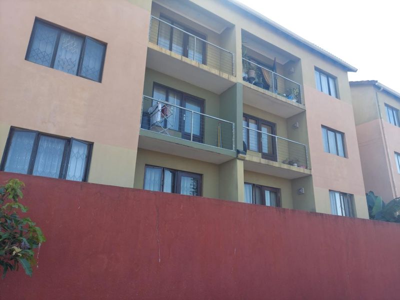 Rear elevation of a multi-story apartment building featuring private balconies with metal railings and sliding glass doors.
