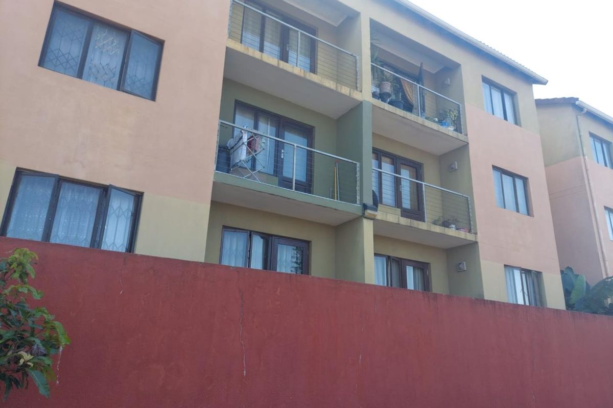 Rear elevation of a multi-story apartment building featuring private balconies with metal railings and sliding glass doors.
