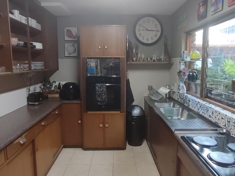 A functional kitchen featuring wood-tone cabinetry, laminate countertops, a double stainless steel sink, and a built-in oven with an electric hob.