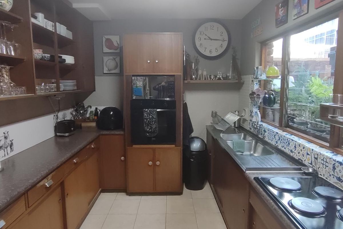 A functional kitchen featuring wood-tone cabinetry, laminate countertops, a double stainless steel sink, and a built-in oven with an electric hob.