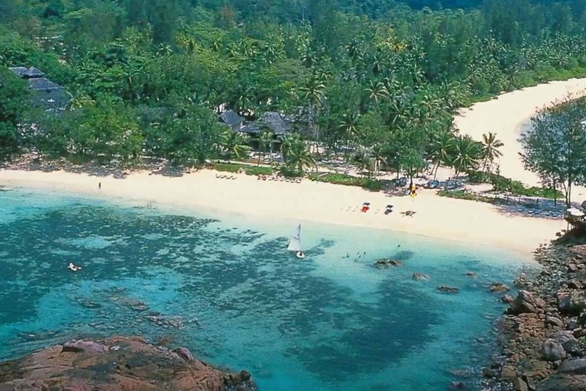 Aerial view of a pristine coastal property featuring white sandy beaches, lush tropical vegetation, and clear turquoise waters.