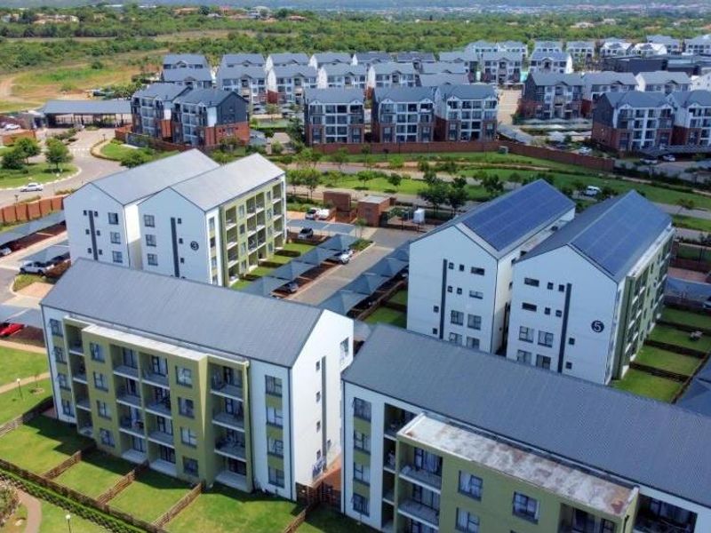 Aerial view of a modern apartment complex featuring multiple residential blocks, solar-equipped pitched roofs, covered parking, and well-maintained communal garden areas.