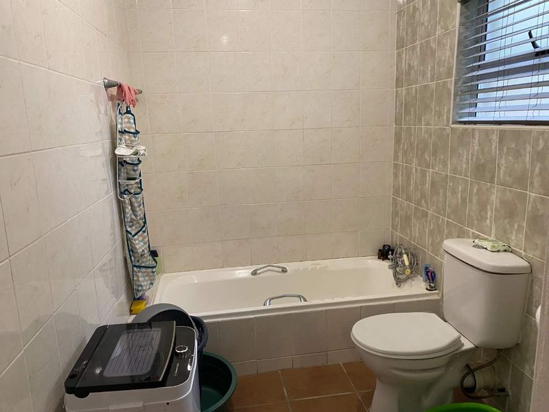 A functional bathroom featuring a built-in bathtub, toilet, and tiled finishes. The space would benefit from cosmetic updates to modernize the fixtures and tiling.