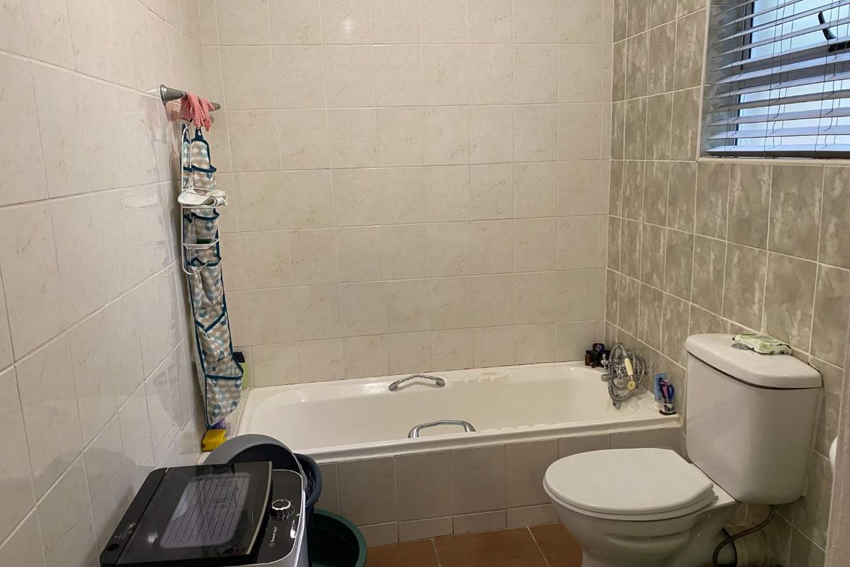 A functional bathroom featuring a built-in bathtub, toilet, and tiled finishes. The space would benefit from cosmetic updates to modernize the fixtures and tiling.