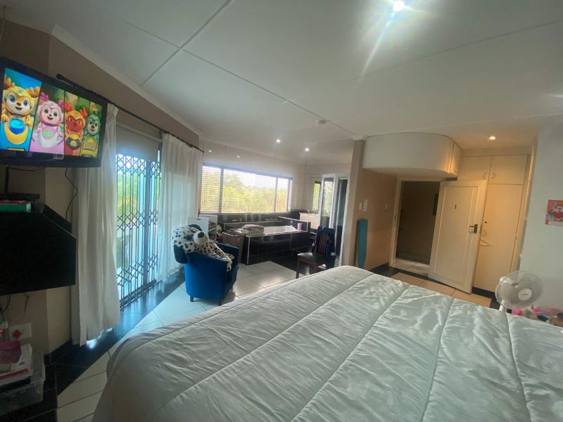 Spacious bedroom featuring tiled flooring, built-in cupboards, and an integrated en-suite bathtub area with large windows and access to a private balcony.