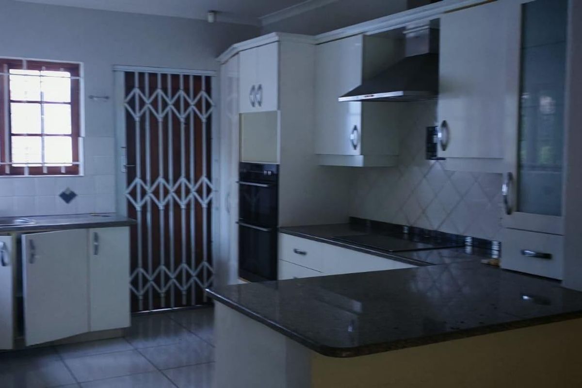 A functional kitchen featuring granite countertops, built-in cabinetry, an integrated oven, and a stainless steel extractor fan, with tiled flooring throughout.