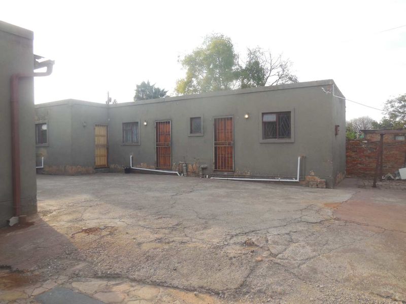Rear exterior view of the apartment building featuring concrete paving, security gates, and external wall finishes showing signs of wear.