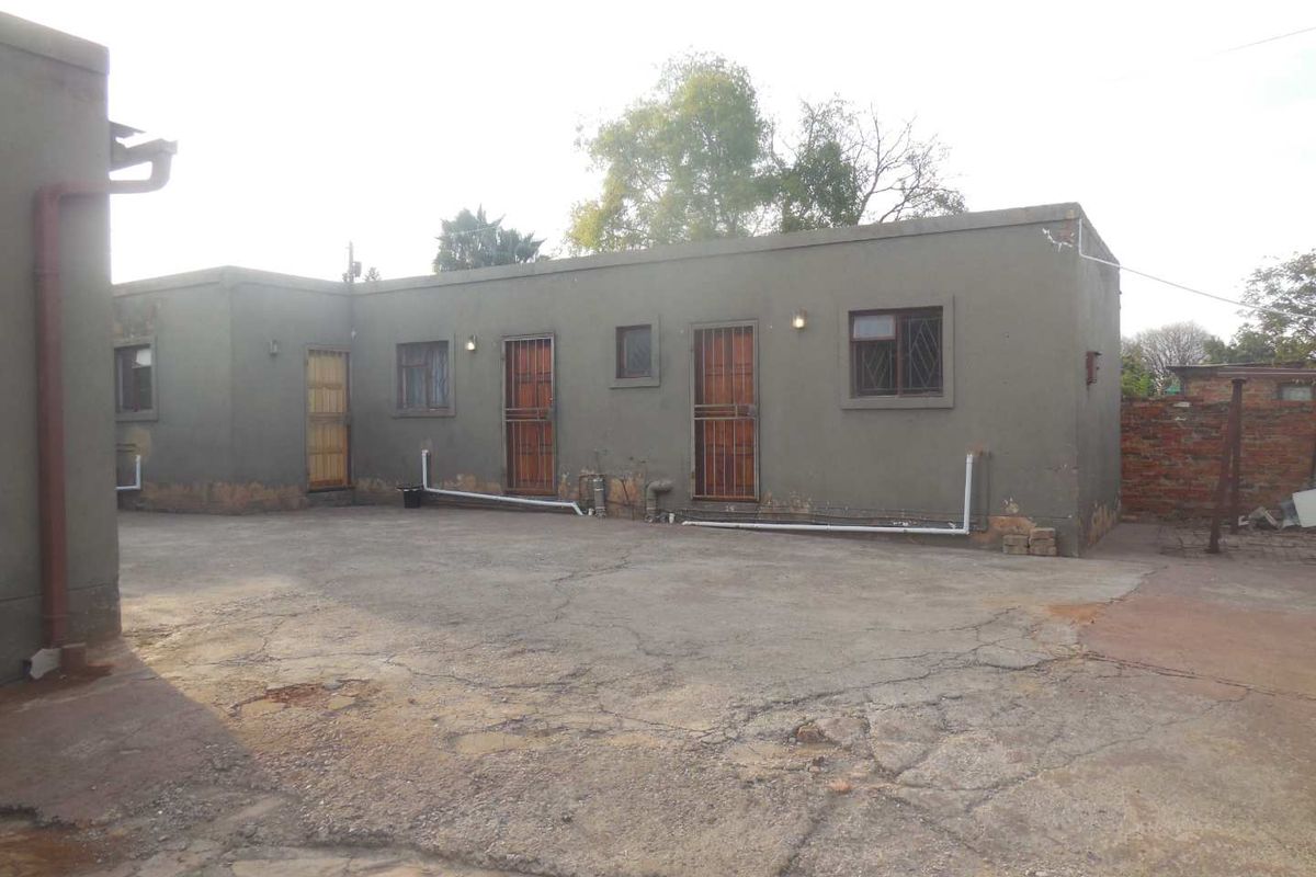 Rear exterior view of the apartment building featuring concrete paving, security gates, and external wall finishes showing signs of wear.