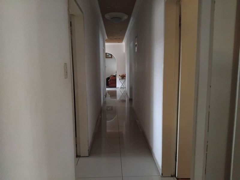 A narrow residential hallway featuring tiled flooring and a recessed ceiling detail, leading towards an arched entryway.