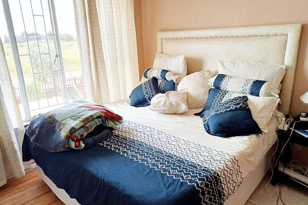 A bedroom featuring a large bed with a headboard, positioned next to a sliding glass door with security bars and natural light.