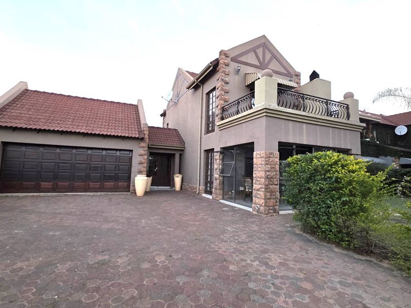 Front elevation of a multi-story house featuring a paved driveway, double garage, stone-clad accents, and an upper-level balcony with wrought iron railings.