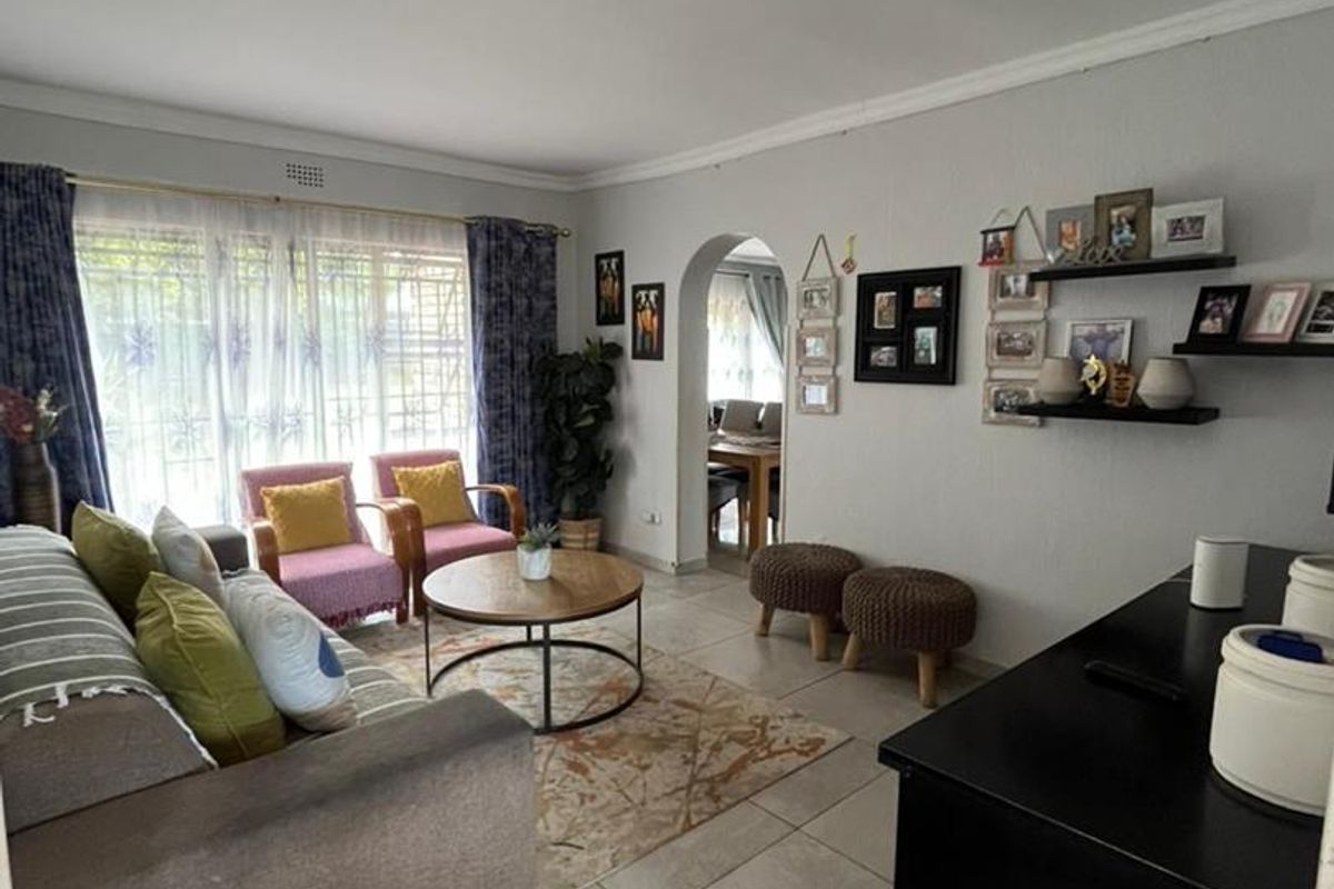 A comfortable living room featuring large windows with security bars, tiled flooring, and an arched doorway leading to the adjacent dining area.