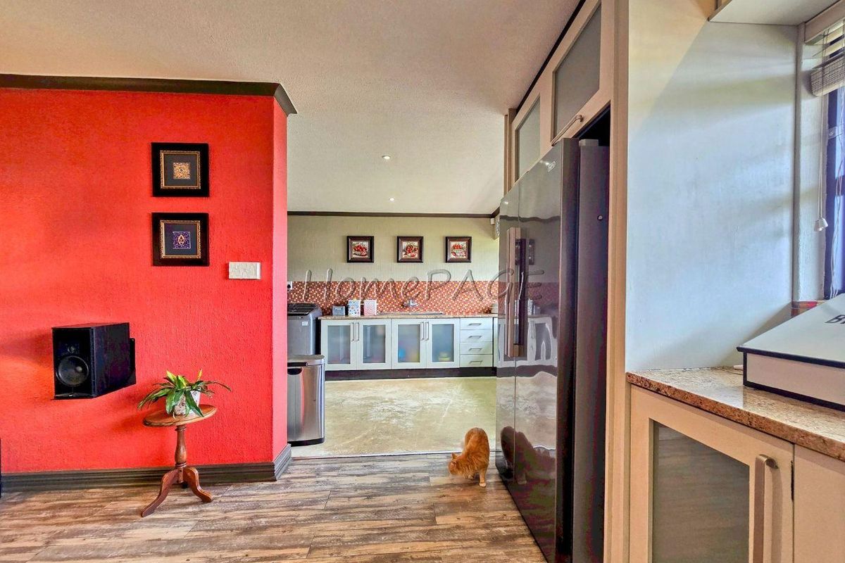 A view of a kitchen area featuring built-in cabinetry, granite countertops, and wood-look flooring, connecting to an adjacent living space with a bold red wall.