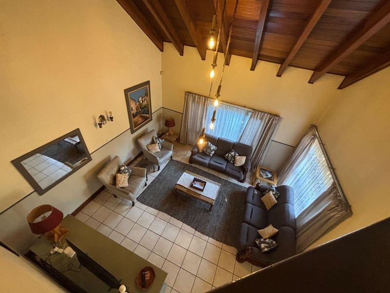 Spacious living room featuring a high vaulted ceiling with exposed timber beams, ceramic tiled flooring, and a classic dado rail finish.