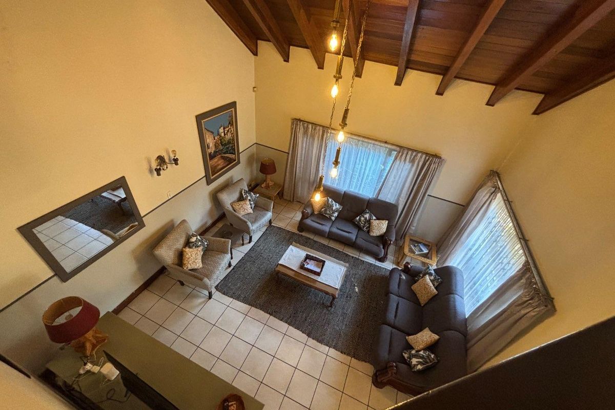 Spacious living room featuring a high vaulted ceiling with exposed timber beams, ceramic tiled flooring, and a classic dado rail finish.